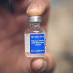 hand holding a flu vaccine vial with a blue label